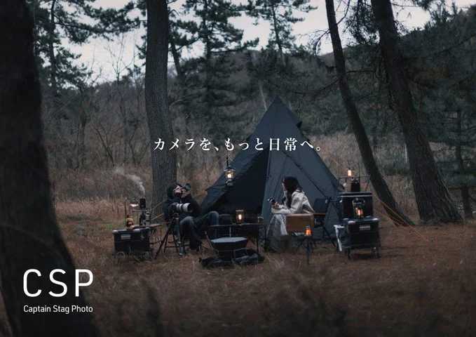 キャンプ場でテントのそばに座りカメラを構える人物とロゴ
