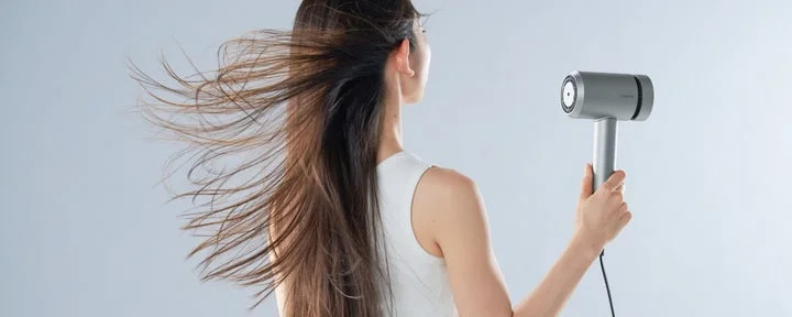 女性がヘアドライヤーを使って髪を乾かしている後ろ姿。