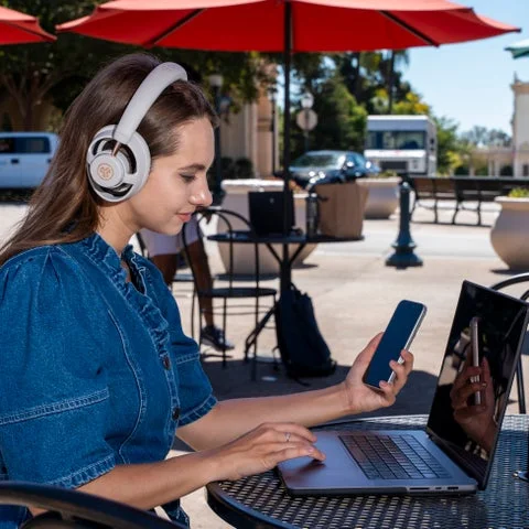 カフェのテラス席でJBuds Open Wirelessを装着しノートPCを操作する女性