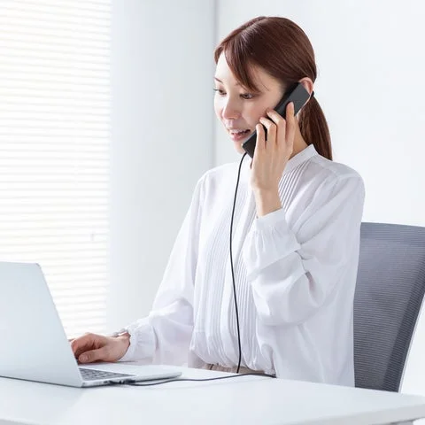 PCに向かって受話器で通話している女性