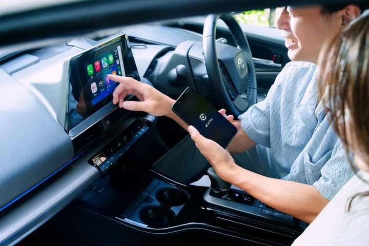 車内でドライバーと助手席の人がワイヤレス接続された画面を操作している様子