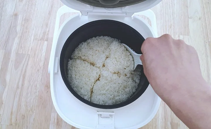 炊飯器のふたを開け、しゃもじで炊き上がったごはんをほぐす様子