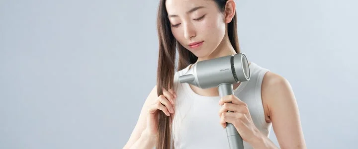 女性がドライヤーを手に持ち、髪をケアしている様子。