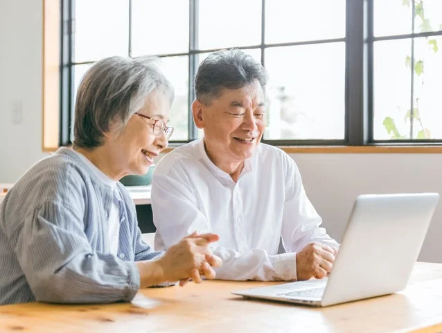 PC画面を一緒に見ながら微笑む高齢の夫婦