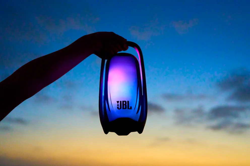 JBL Pulse 6のハンドルを手に持ち、夕暮れの空を背景にLEDが点灯している様子