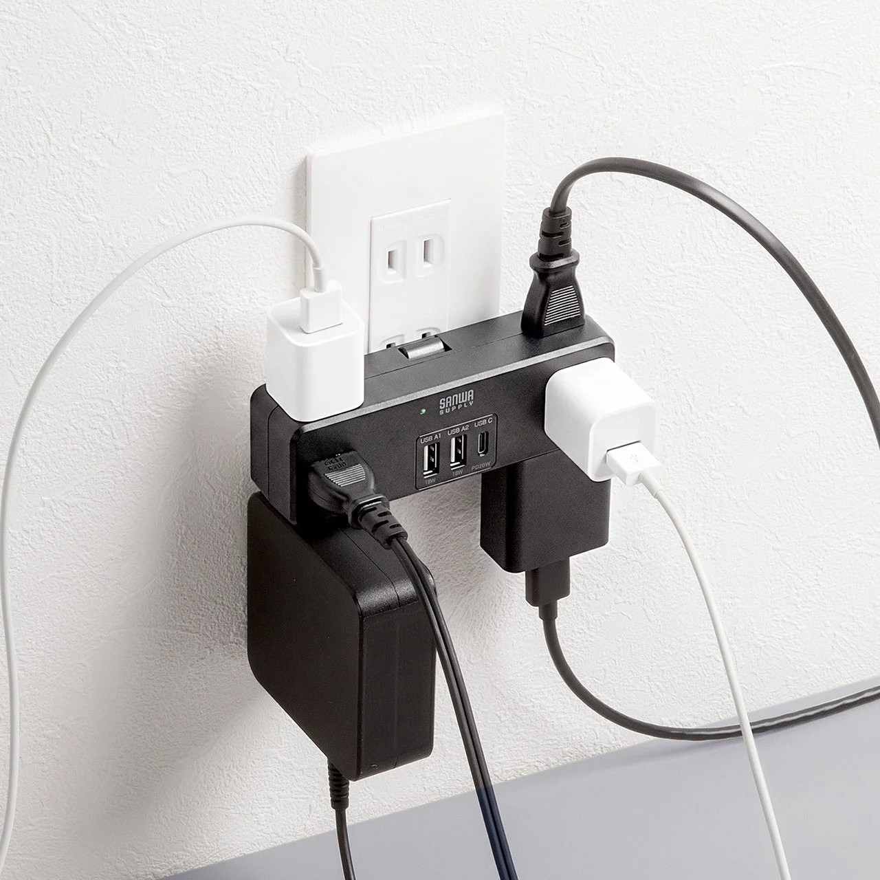 700-TAP093BKの黒色直挿し式電源タップが壁のコンセントに接続され、USBポートにケーブルが挿された状態