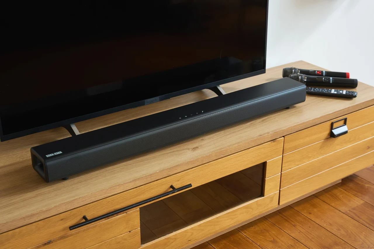 テレビ下の木製家具に置かれたKARA×KARAサウンドバーとマイク