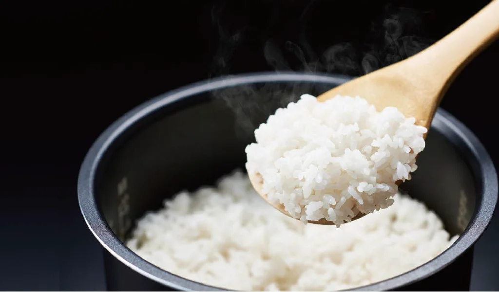 炊き上がったご飯を木製お玉で掬い上げ、釜から立ち上る湯気が見えるイメージ