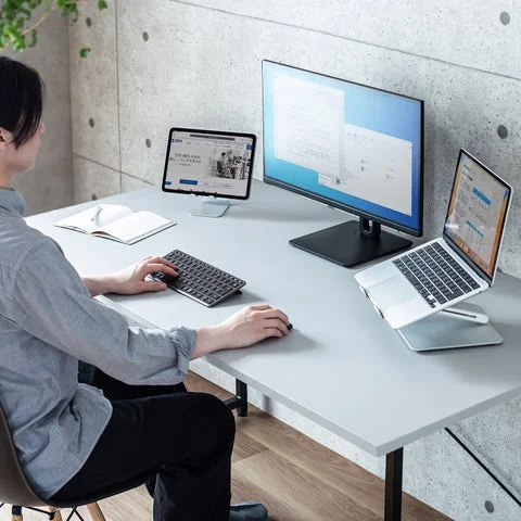 デスクでパソコン、タブレット、キーボードを使用して作業する様子