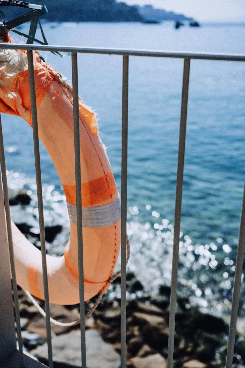 手すりに掛かったオレンジ色の救命浮環と、奥に広がる海と岩場の風景