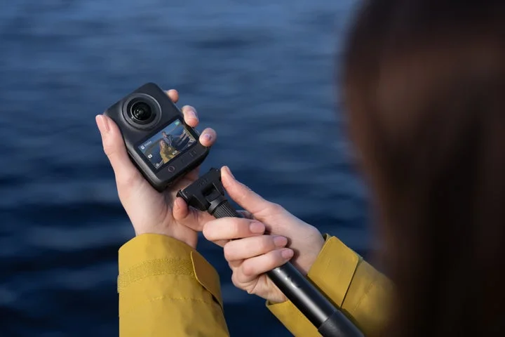 水辺でセルフィースティックに装着したOsmo 360 IIを手に持ち、画面を確認する人物