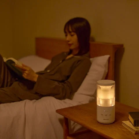 夜のベッドサイドでライトが点灯している加湿器と読書をする女性