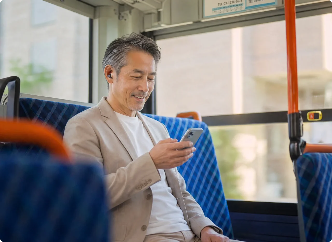 Cearvol Wave装着の男性がバス内でスマートフォンを操作する様子