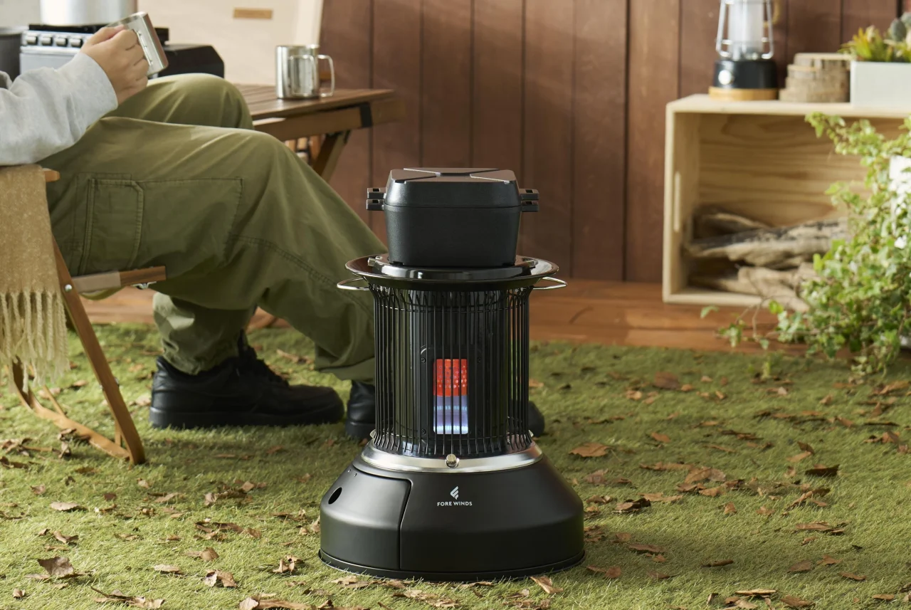 カセットガスストーブ「マル暖プラス」の屋外使用イメージ。芝生の上に置かれ、人物が横でくつろいでいる。