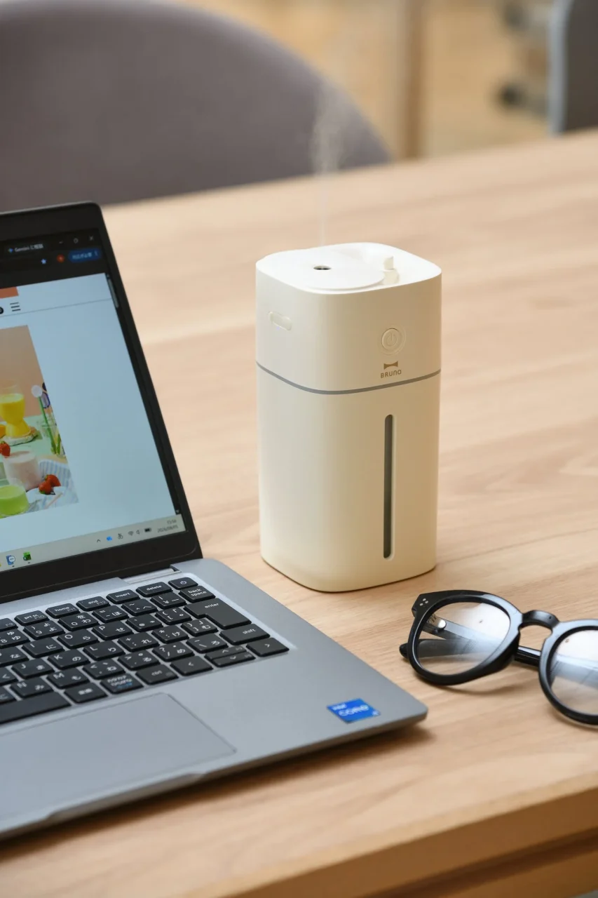 上部給水コードレス加湿器。ノートPCや眼鏡の横に置かれた、ミストを噴出するベージュ色のコンパクトな加湿器。