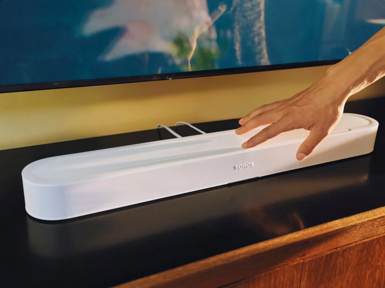 テレビ下に設置された白いSonos Beam Ultraサウンドバーと、その上に置かれた手
