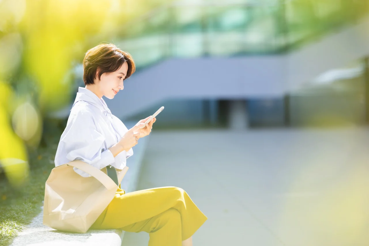 屋外で座り、スマートフォンを操作する女性