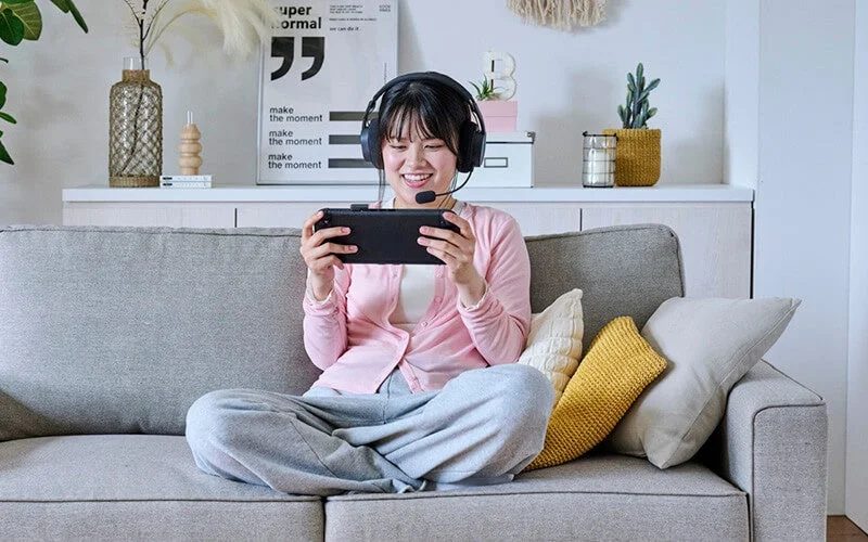 ソファでゲーム機を操作しながら、フレキシブルアームのマイクでボイスチャットを楽しんでいる女性