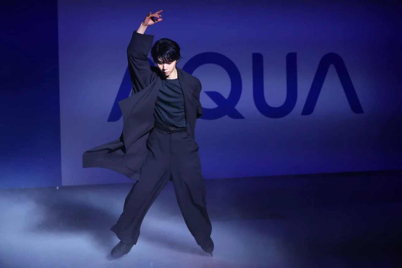 青い照明とスモークの中、氷上で片腕を上げる羽生結弦さん