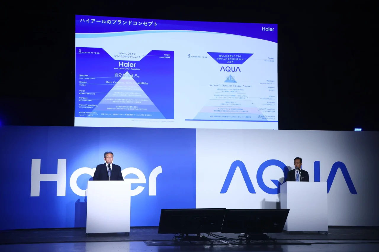 ブランドコンセプトのスクリーンを背に、2人が演台に立つ企業パート
