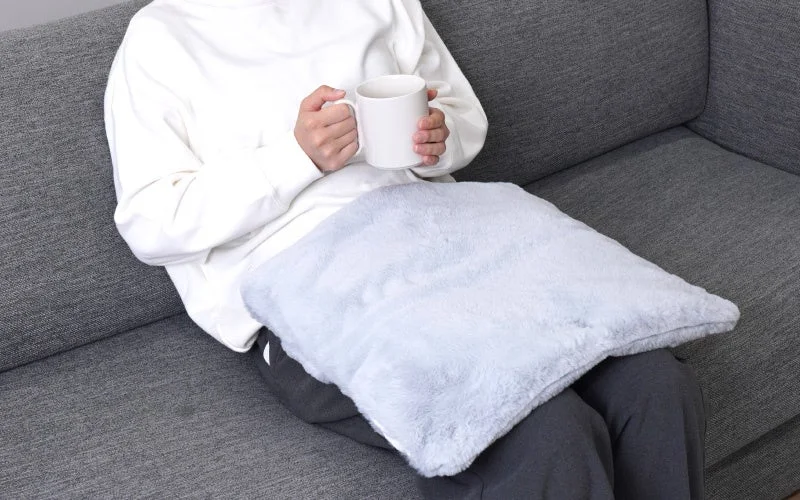 ソファでマグカップを持ち、膝にふわふわのおなかぽかぽかポッケを広げた人