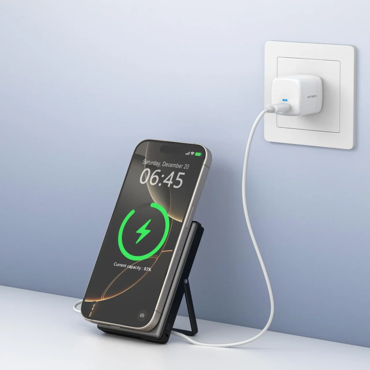 角度調整スタンドでスマホを立てて充電する様子。壁のコンセントに白い充電器