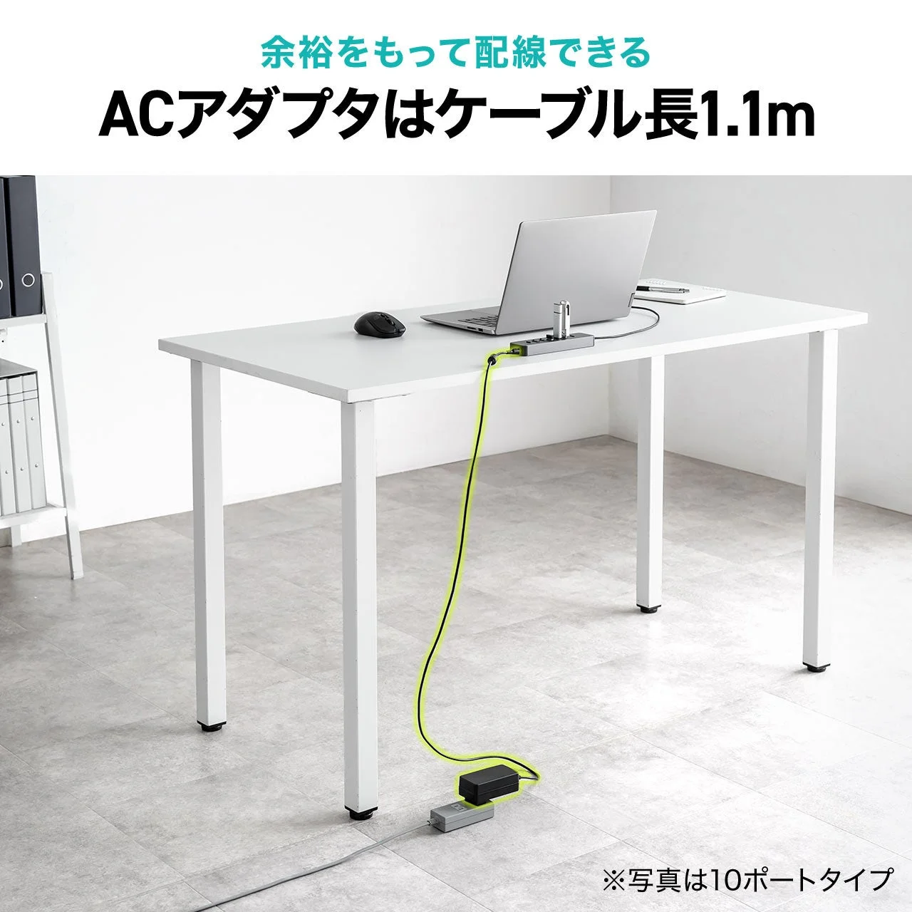 白いデスク上のノートPCとUSBハブへ、床の電源タップから延びるACアダプタのケーブル
