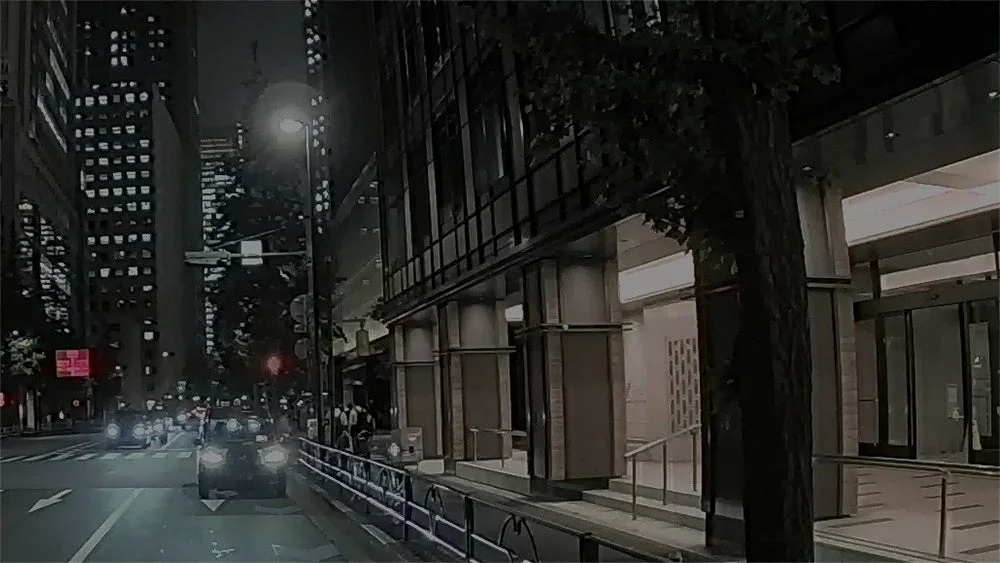 夜の市街地の後方映像イメージ。ビル街の道路を走る車と街灯が見える