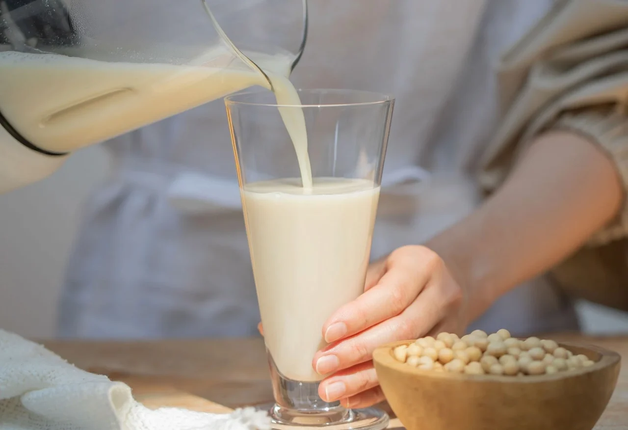 まるごと豆乳をグラスに注ぐ様子と大豆の入った木製ボウル