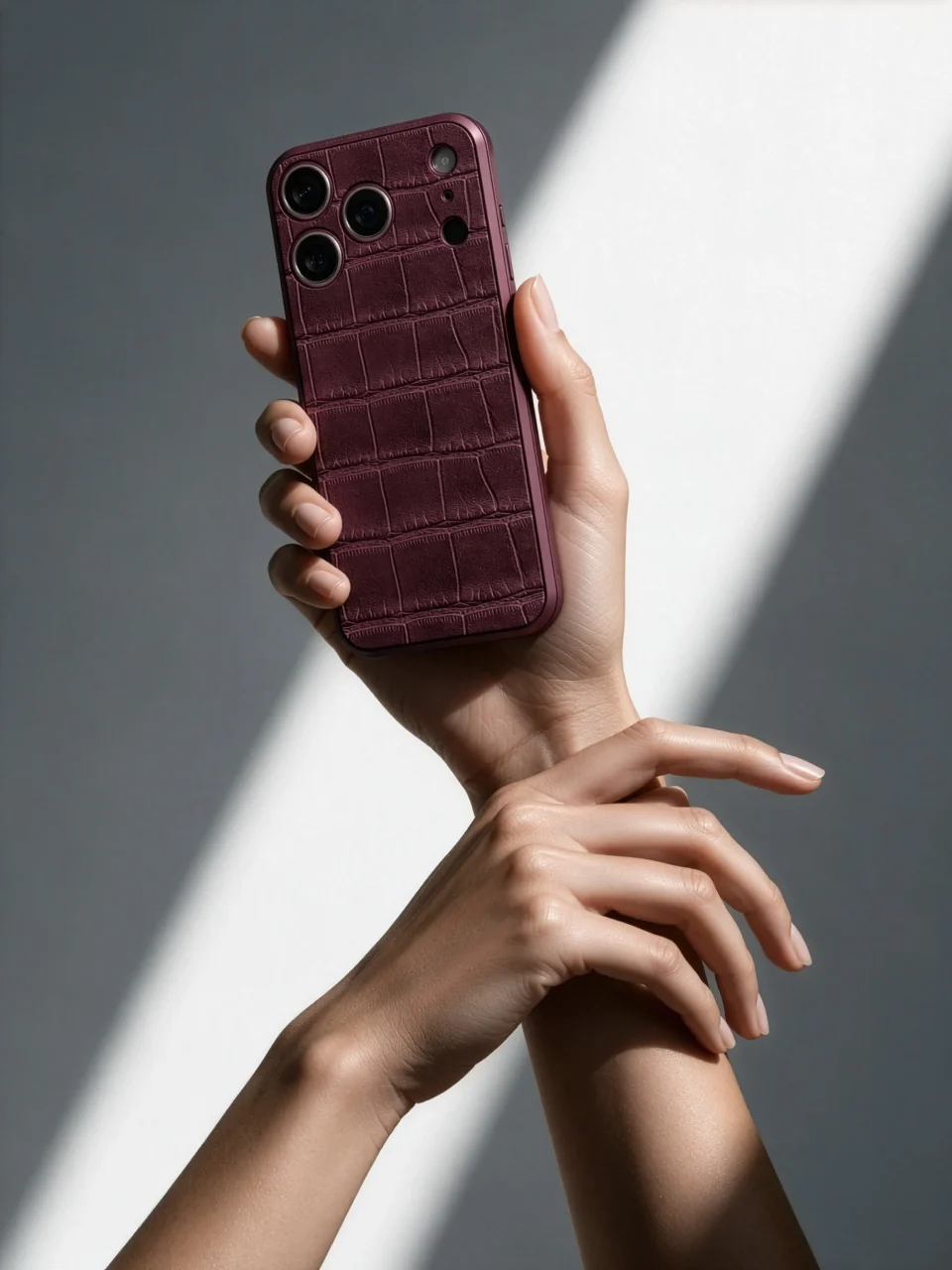 Croco Embossed Magnetic Shieldを付けたバーガンディ色のiPhoneを持つ手