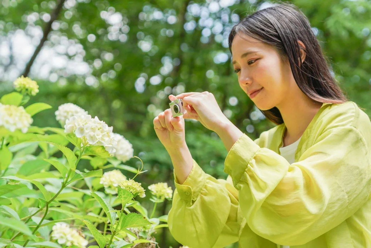 トイカメラ Pieni IIIを手に持ち、花を撮影する女性
