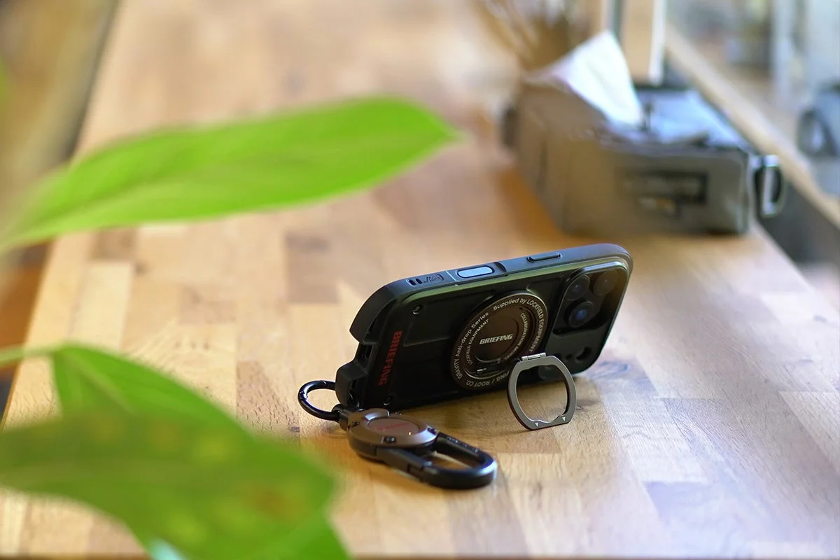 木のテーブルに置かれた黒いスマホケースとカラビナ、リング