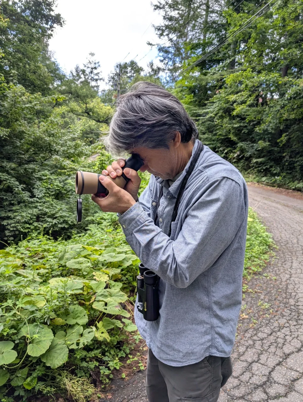 首に双眼鏡を下げ、小型スコープをのぞく男性
