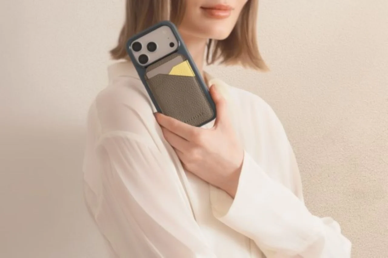 レザーのカードケースを背面に付けたスマホを持つ白いシャツの女性