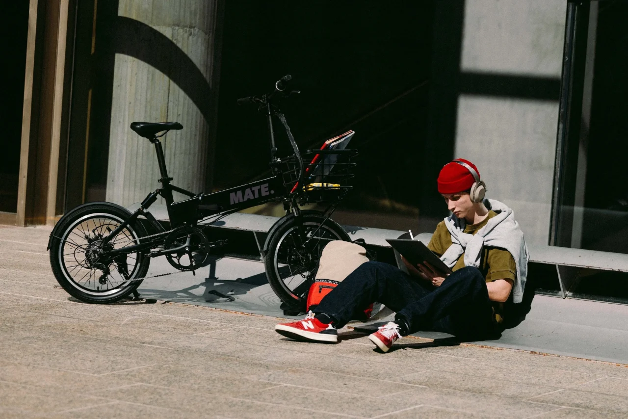 MATE City 2.0。黒い折りたたみ型e-BIKEの横で座って過ごす人