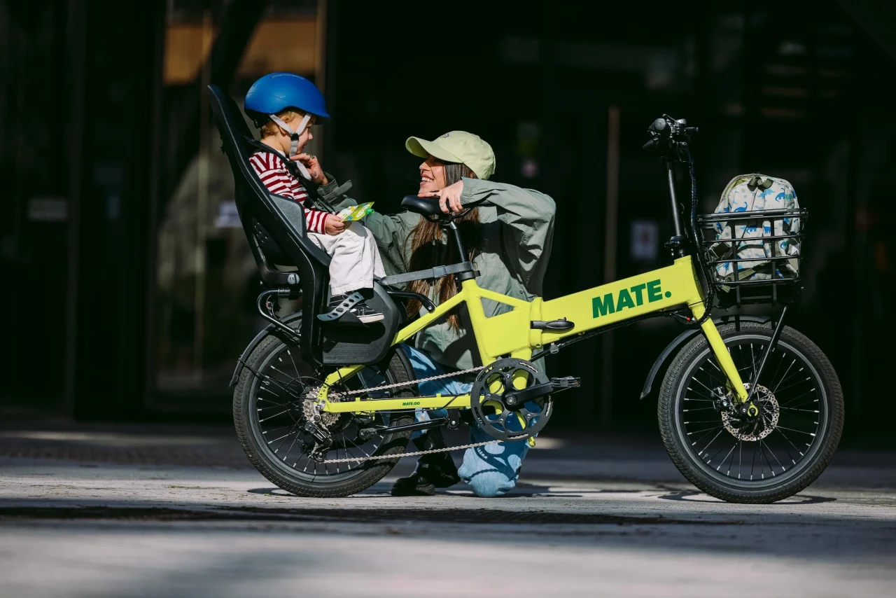 MATE GO+。黄緑色のフレームに後部チャイルドシートを付けた自転車と、そばで笑う親子