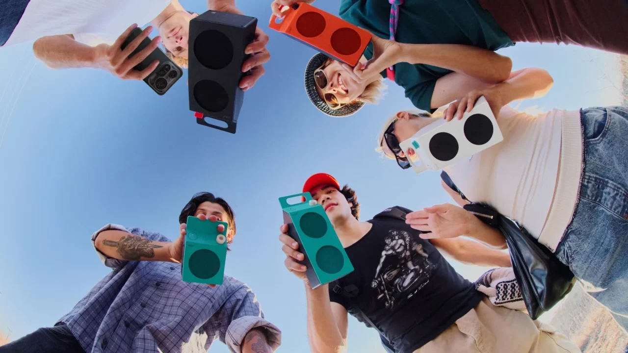 下から見上げる構図で、5人がCMF Speakerのポータブルスピーカーを手に持つ