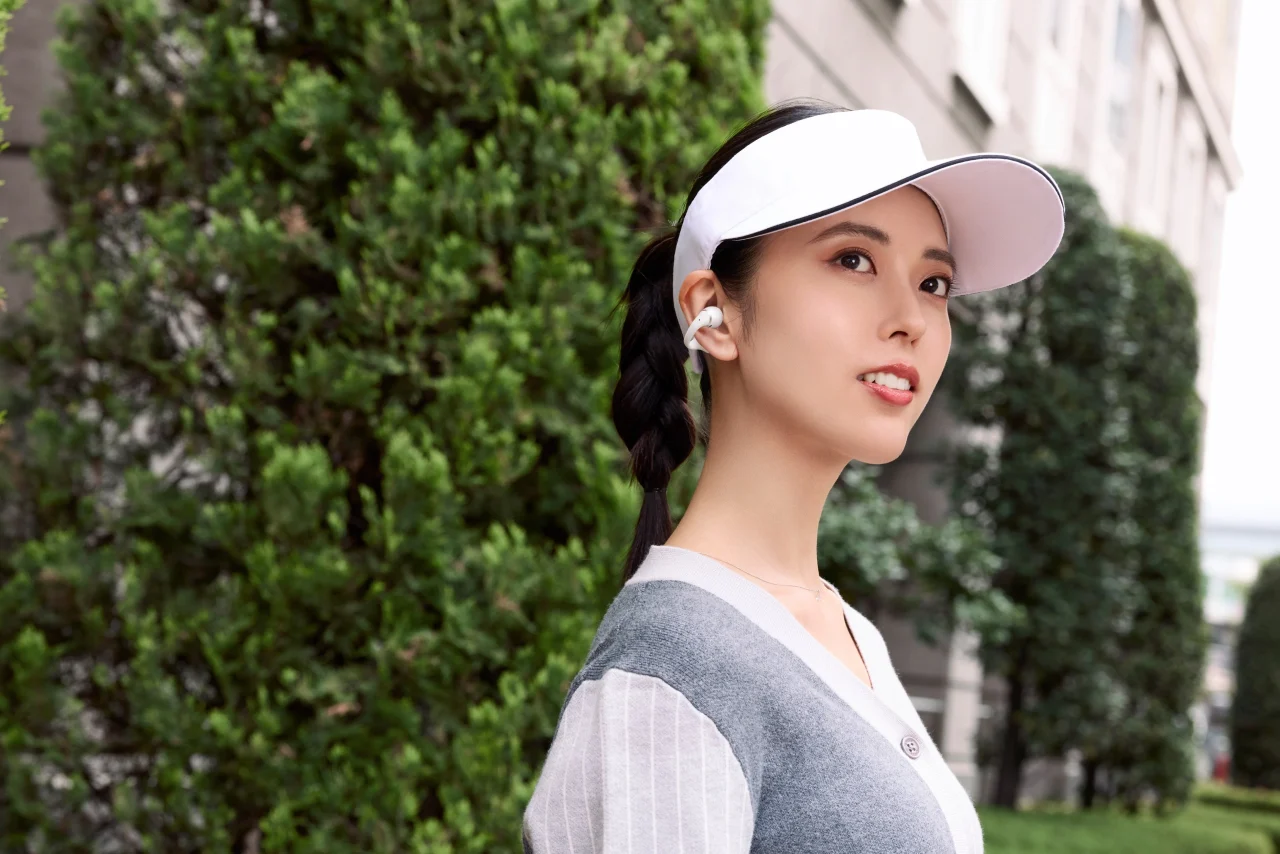 白いバイザーをかぶり耳にイヤーカフ型イヤホンを着けた女性