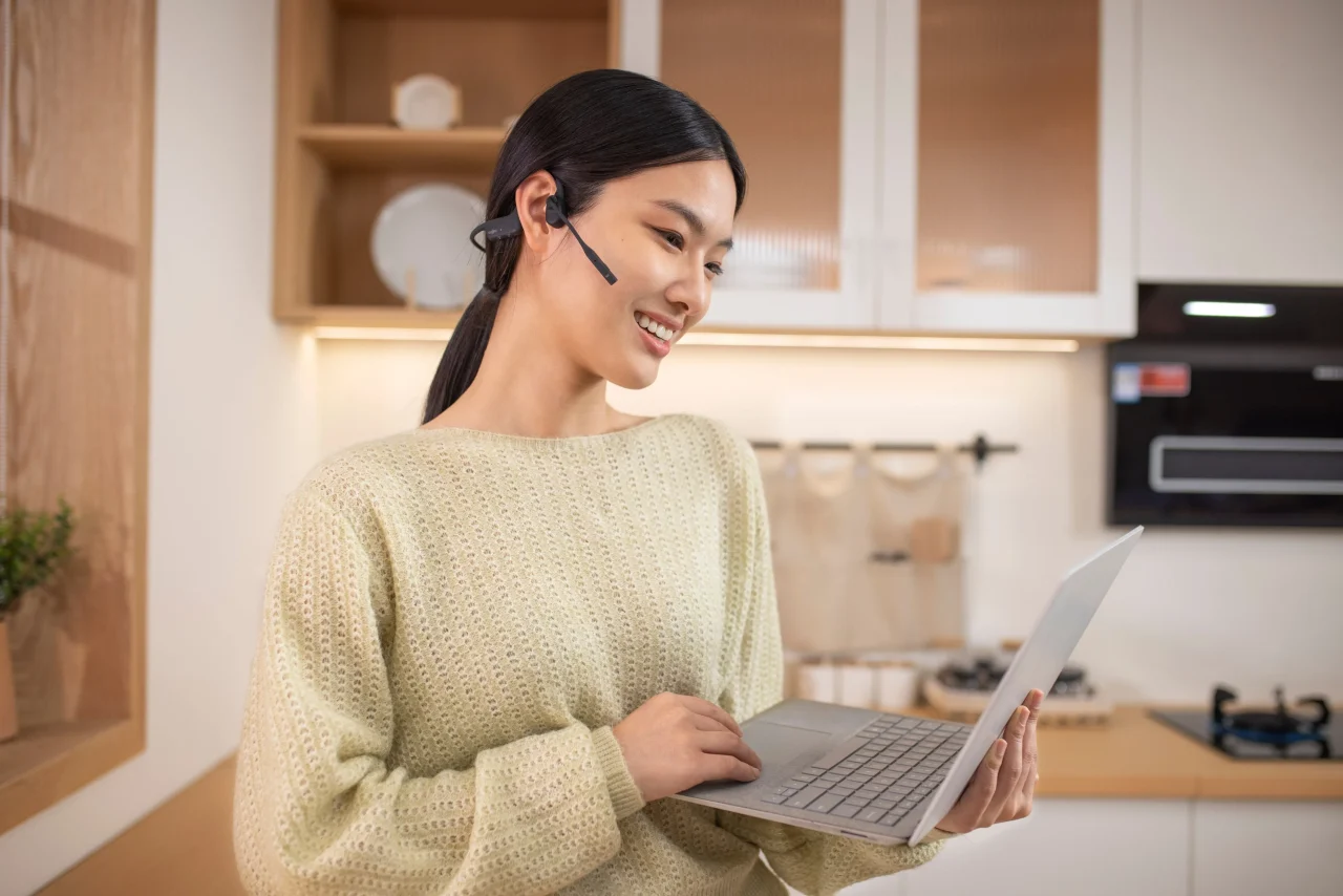 ビジネス向け・ヘッドセットを装着し、ノートPCを持って微笑む女性