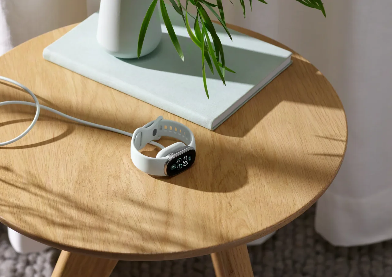 Google Fitbit Edge を充電している様子。木製サイドテーブル上のケーブル接続