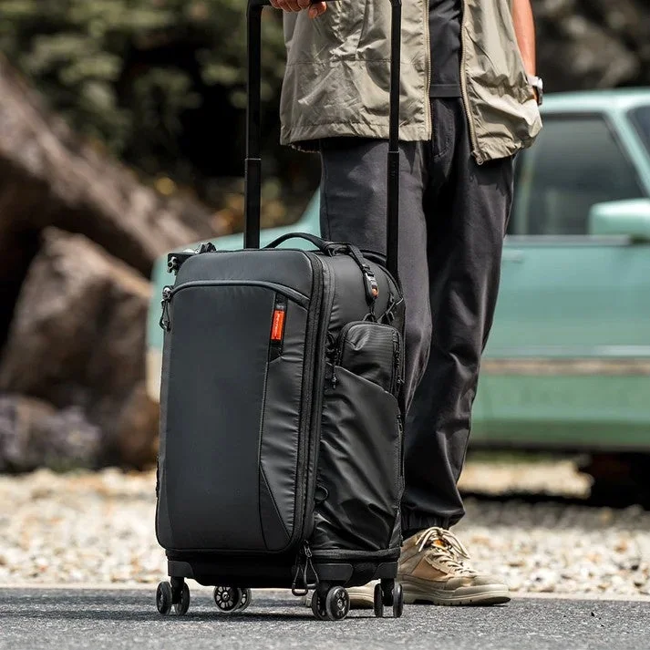 Roller Camera Backpack。伸ばしたハンドルとキャスター付きの黒いバッグを引く人