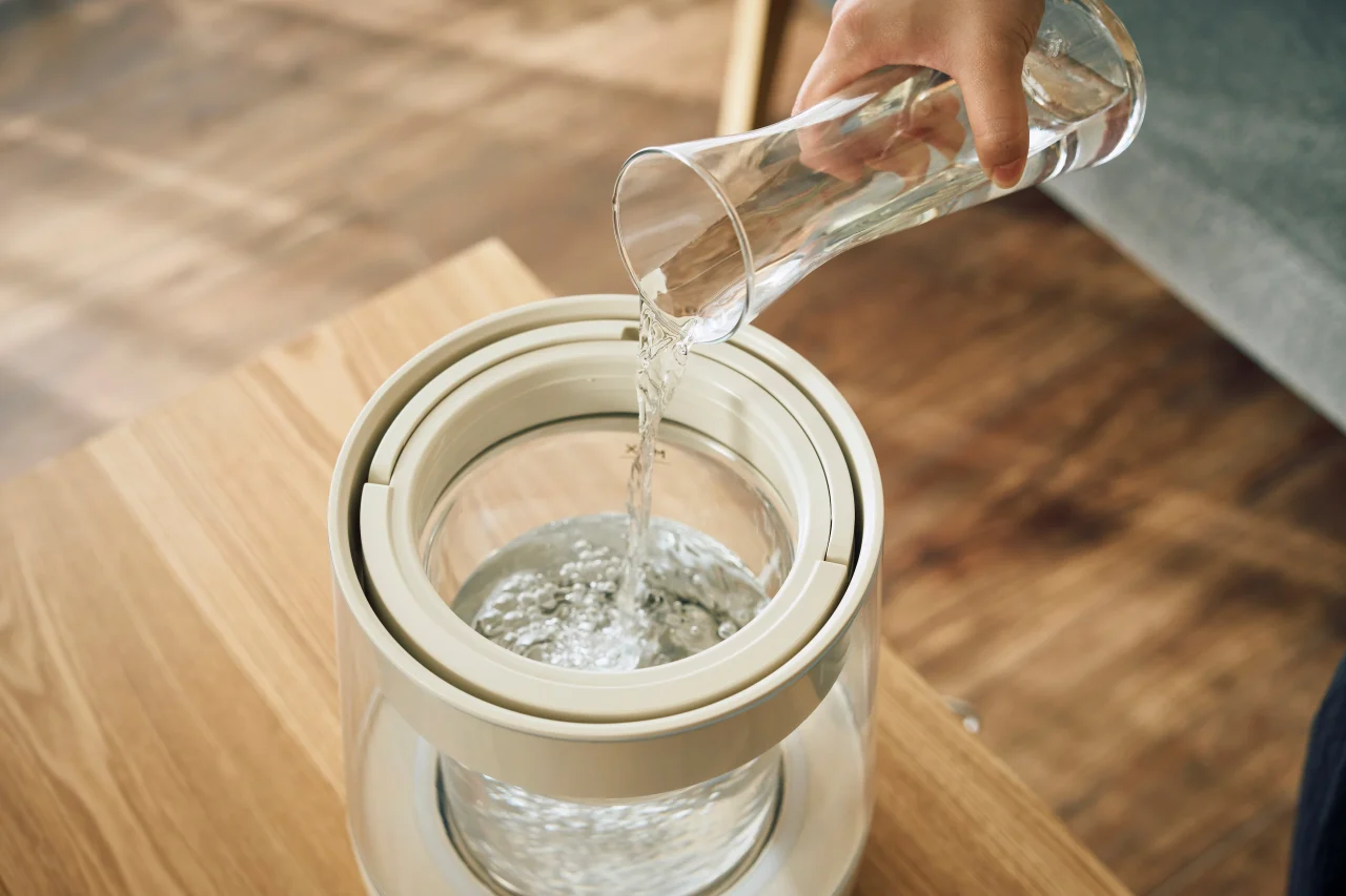 ガラス製の水差しから加湿器のガラスポットへ上から水を注ぐ様子