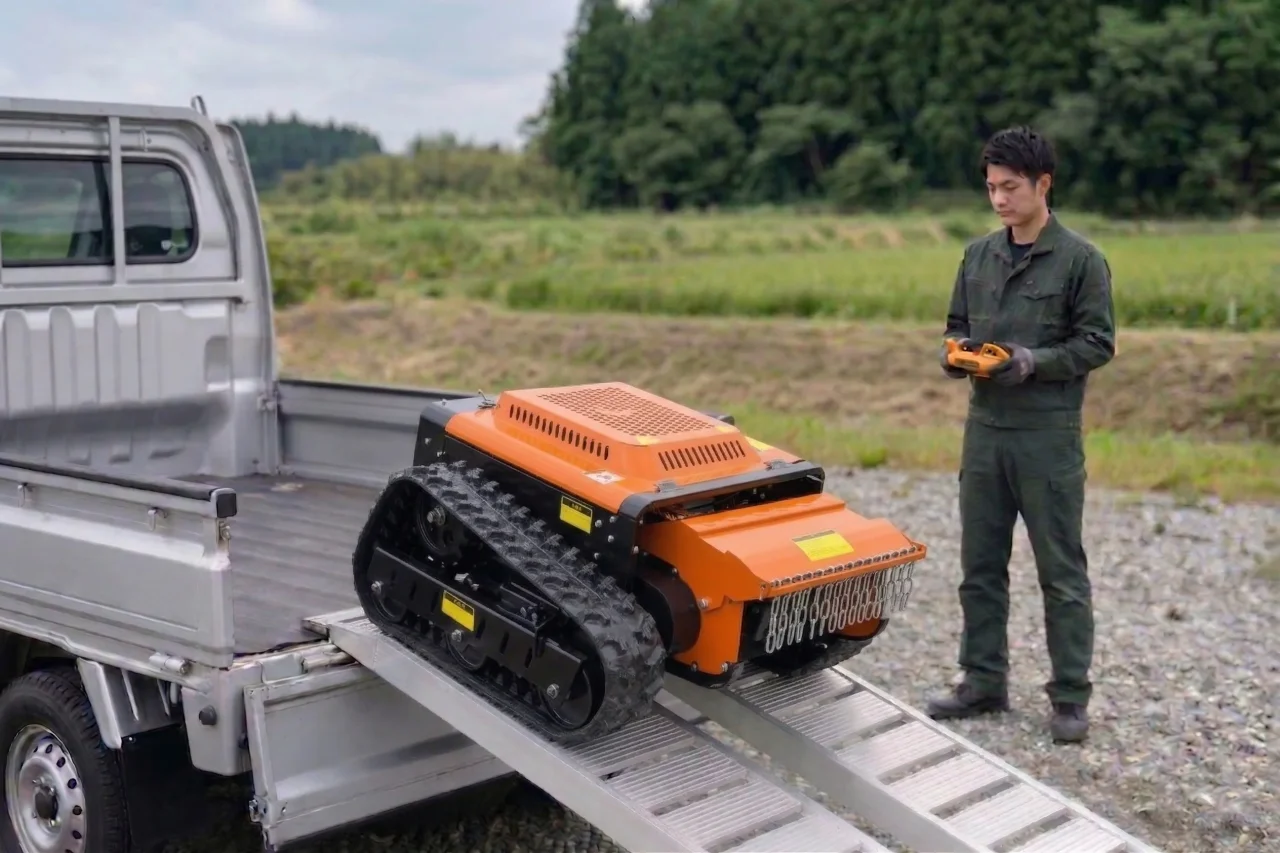 トラックの荷台からラジコン草刈機をリモコン操作で降ろす作業者