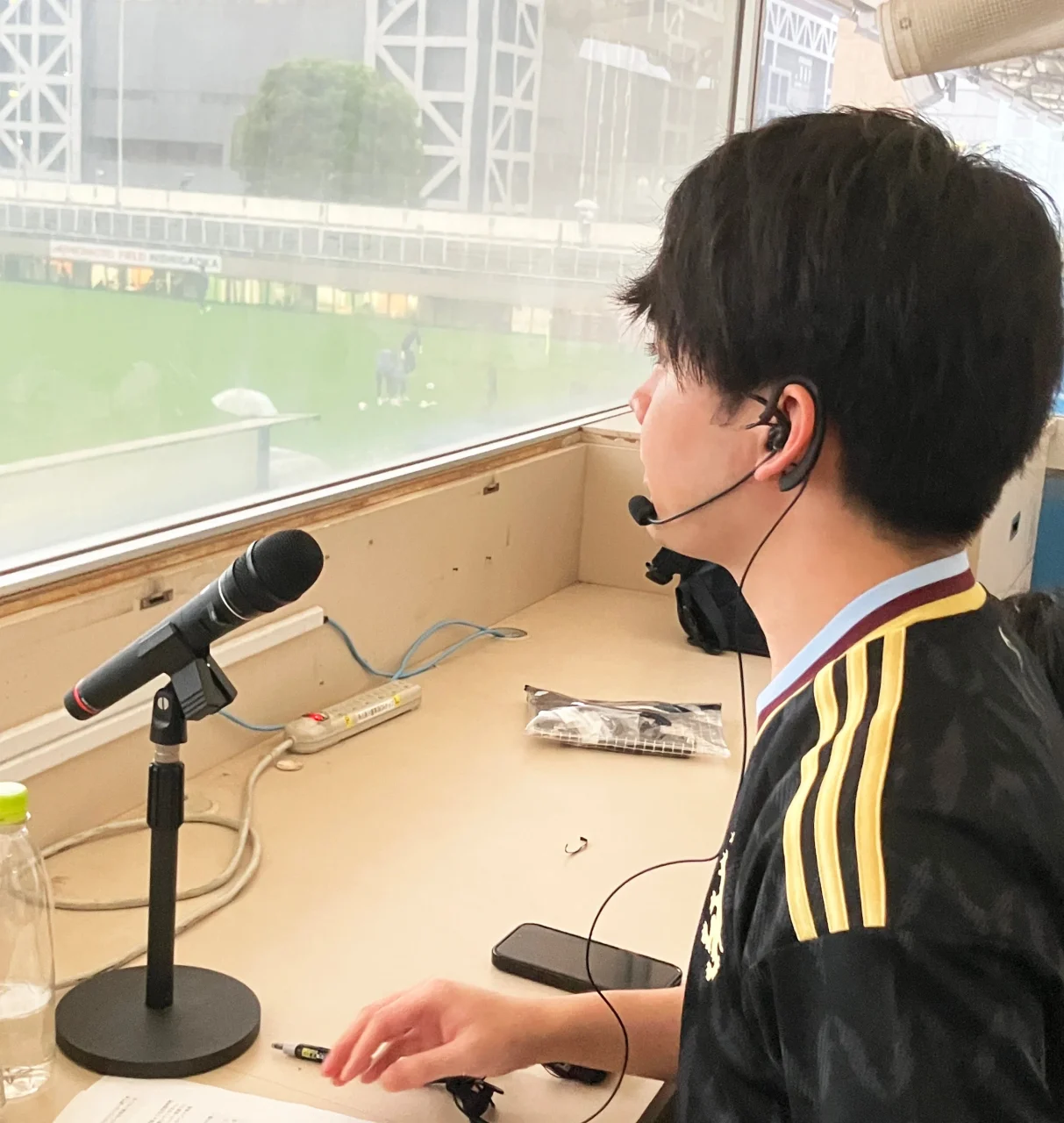 実況席でマイクとイヤホンマイクを使い実況する人物