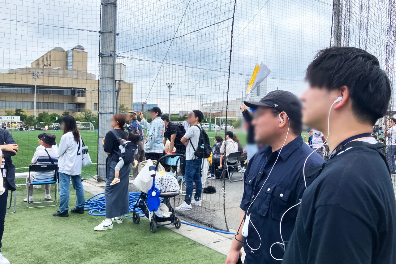 ガイドフォンのイヤホンを着けて屋外で試合を観戦する観客たち