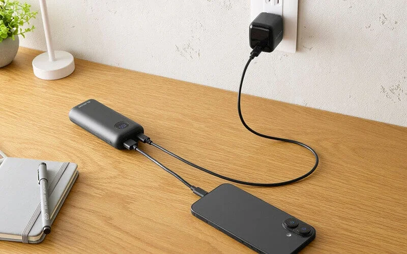 パススルー充電中の黒いモバイルバッテリーとスマートフォン、コンセントの充電器