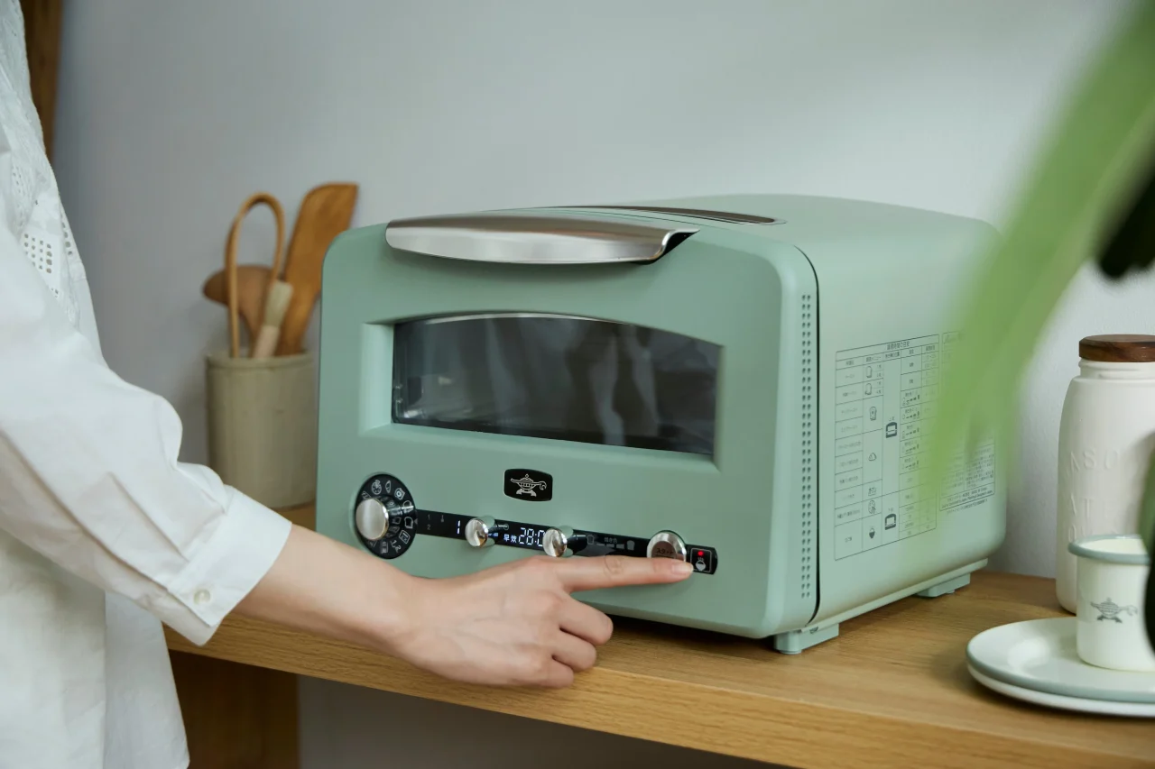 木製カウンター上のグリーンのグラファイト グリル&トースターを操作する手元