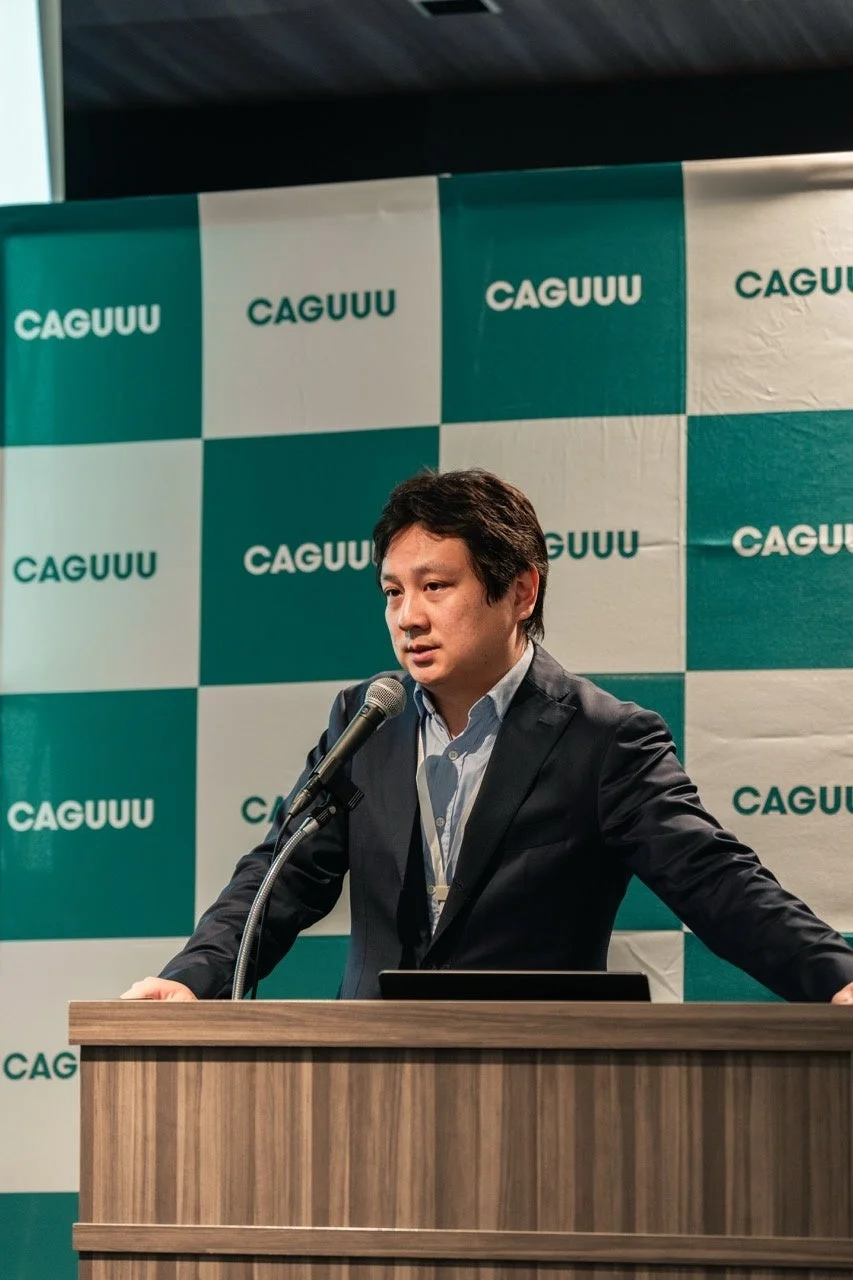 CAGUUUの背景の前で登壇する代表取締役社長・中村勇輝