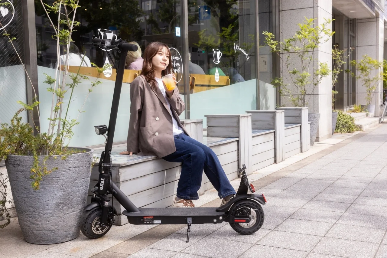 街中のベンチ脇に置かれたeXs 1 TKGの電動キックボードと女性