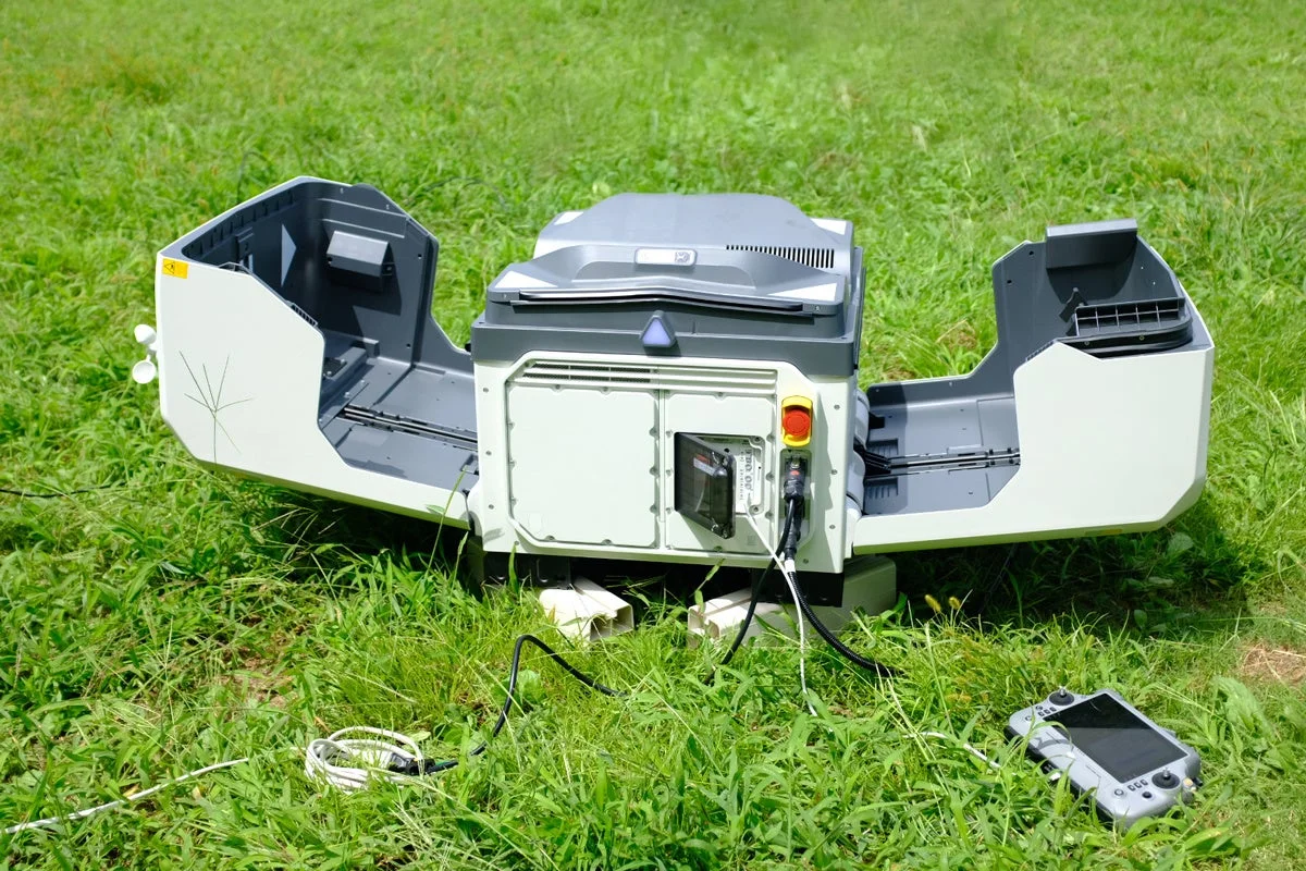 芝生の上に置かれた、両側のカバーが開いたDJI Dock 4と操作端末